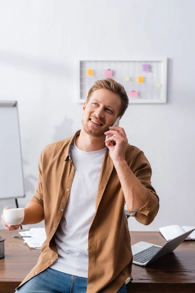 Geschäftsmann in legerer Kleidung hält Tasse Kaffee in der Hand, während er mit dem Handy spricht — Stockfoto