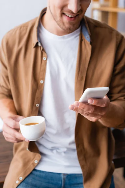 Vista recortada de mensajería de hombre de negocios en el teléfono inteligente mientras sostiene la taza de café - foto de stock