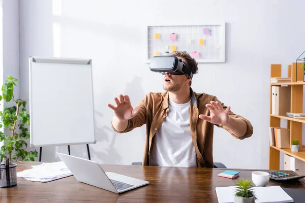 Aufgeregter Geschäftsmann gestikuliert, während er am Arbeitsplatz das vr-Headset benutzt — Stockfoto