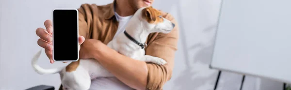 Частичный взгляд бизнесмена, показывающего смартфон с пустым экраном, держа в руках собаку-терьера Джека Рассела, панорамный снимок — стоковое фото