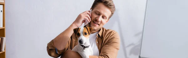 Horizontal concept of businessman talking on mobile phone and holding jack russell terrier dog — Stock Photo