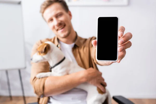 Selective focus of businessman showing smartphone with blank screen while holding jack russell terrier dog — Stock Photo