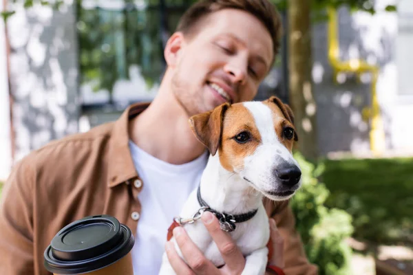 Selective focus of young man holding jack russell terrier dog and coffee to go — Stock Photo