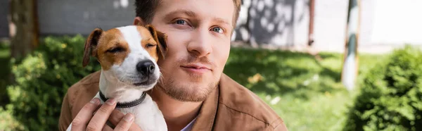 Panoramic shot of man cuddling jack russell terrier dog while looking at camera — Stock Photo