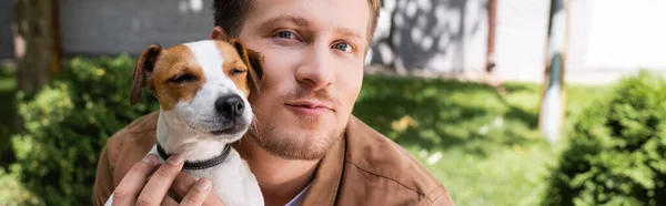 Panoramaaufnahme eines Mannes, der Jack Russell Terrier Hund knuddelt, während er in die Kamera schaut — Stockfoto