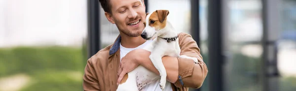 Panoramic concept of young man holding jack russell terrier dog outdoors — Stock Photo