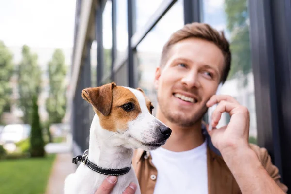 Junger Mann spricht mit Smartphone, während er Jack-Russell-Terrier-Hund auf der Straße hält — Stockfoto