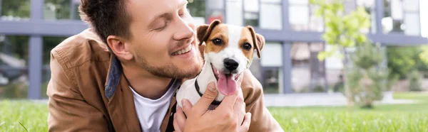 Horizontal concept of man cuddling jack russell terrier dog while lying on grass — Stock Photo