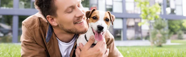 Conceito horizontal de homem abraçando jack russell terrier cão enquanto deitado na grama — Fotografia de Stock