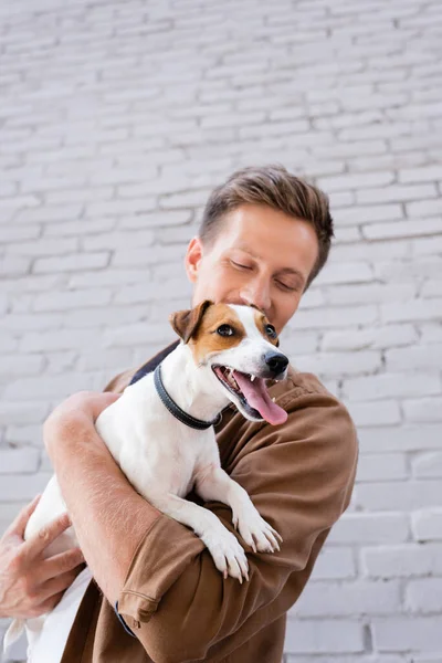 Selective focus of young man holding jack russell terrier near building — Stock Photo