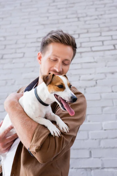 Selective focus of man holding jack russell terrier with sticking out tongue near building — Stock Photo