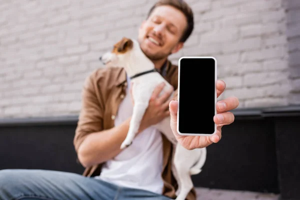 Selective focus of young man holding smartphone with blank screen and jack russell terrier on urban street — Stock Photo
