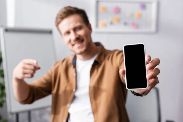 Selektiver Fokus des Geschäftsmannes, der mit dem Finger auf Smartphone mit leerem Bildschirm im Büro zeigt — Stockfoto