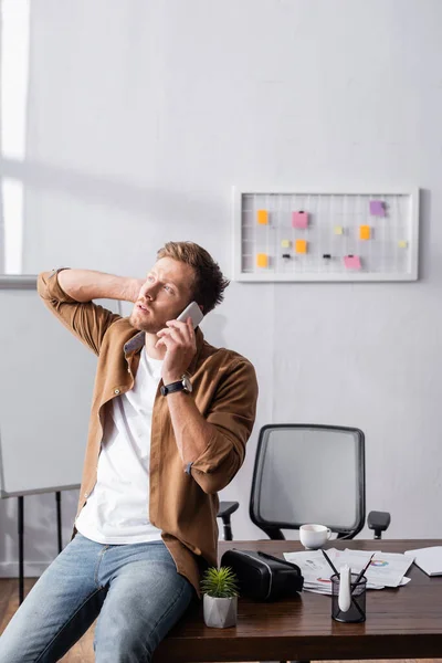 Thoughtful businessman talking on cellphone near vr headset and papers in office — Stock Photo