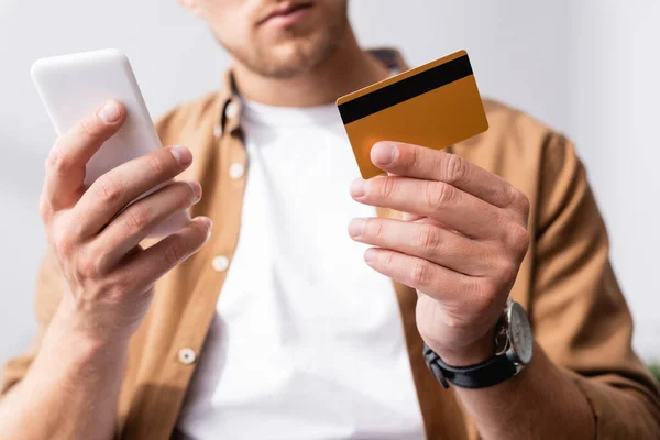 Enfoque selectivo del hombre de negocios con tarjeta de crédito mientras usa el teléfono inteligente en la oficina - foto de stock