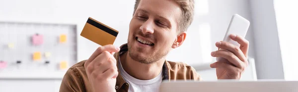 Horizontal concept of businessman looking at credit card while using smartphone in office — Stock Photo