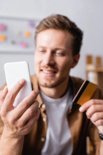 Enfoque selectivo del joven empresario que usa un teléfono inteligente mientras sostiene la tarjeta de crédito - foto de stock