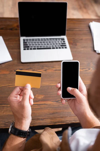 Focus sélectif de jeune homme d'affaires utilisant smartphone et carte de crédit à table — Photo de stock