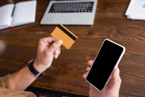 Enfoque selectivo del empresario que sostiene el teléfono inteligente y la tarjeta de crédito mientras trabaja en la oficina - foto de stock