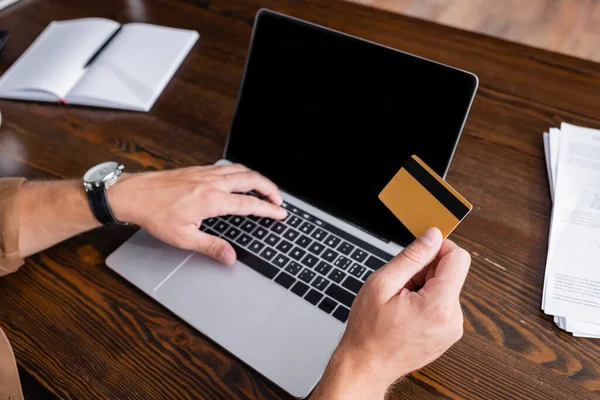 Vista recortada del hombre de negocios con tarjeta de crédito y el uso de la computadora portátil cerca de los papeles en la oficina - foto de stock