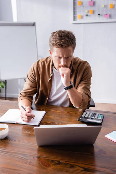 Вибірковий фокус стомлюючого бізнесмена, який дивиться на ноутбук під час написання на ноутбуці в офісі — стокове фото