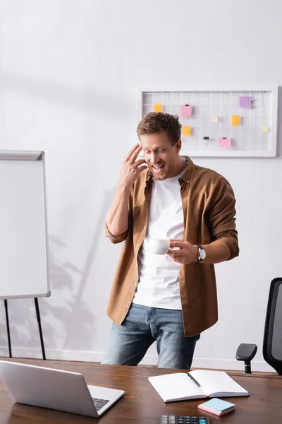 Selective focus of businessman with cup of coffee looking at laptop in office — Stock Photo