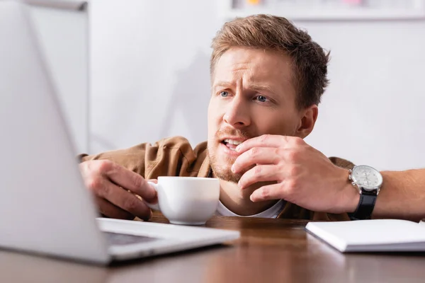 Вибірковий фокус зосередженого бізнесмена з чашкою кави, що дивиться на ноутбук за столом — стокове фото