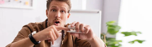 Panoramic shot of excited businessman holding finger near stapler in office — Stock Photo