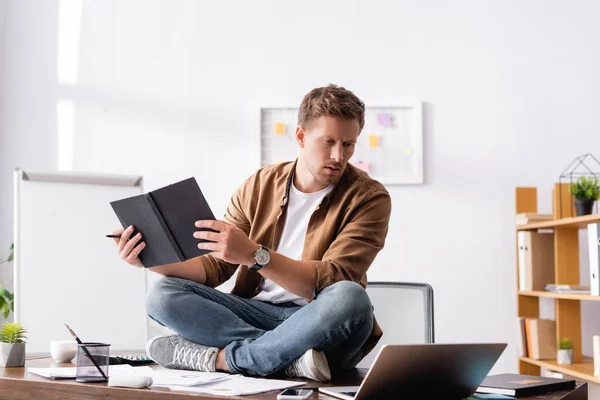 Вибірковий фокус бізнесмена, який тримає ручку і зошит під час сидіння біля ноутбука і паперів на офісному столі — стокове фото