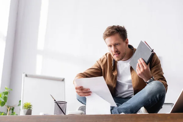 Enfoque selectivo del hombre de negocios que trabaja con papeles y cuaderno mientras está sentado en la mesa en la oficina - foto de stock