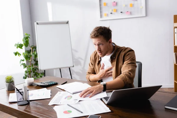Selective focus of businessman touching chest while feeling hurt in office — Stock Photo