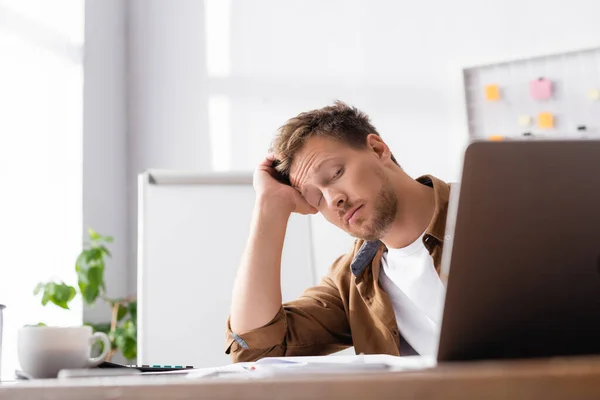 Enfoque selectivo del hombre de negocios agotado mirando el ordenador portátil en la mesa de oficina - foto de stock