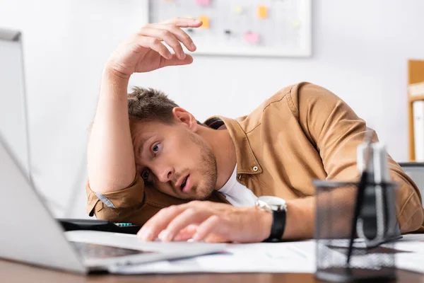 Focus selettivo di affaticato uomo d'affari che utilizza laptop vicino alle scartoffie sul tavolo — Foto stock