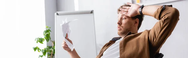 Panoramic shot of tired businessman holding paperwork in office — Stock Photo
