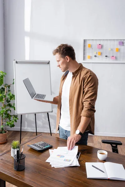 Focus selettivo dell'uomo d'affari che tiene laptop e documenti mentre lavora in ufficio — Foto stock