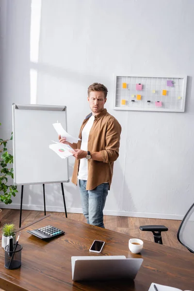 Селективный фокус задумчивого бизнесмена, держащего документы и смотрящего на ноутбук на офисном столе — стоковое фото