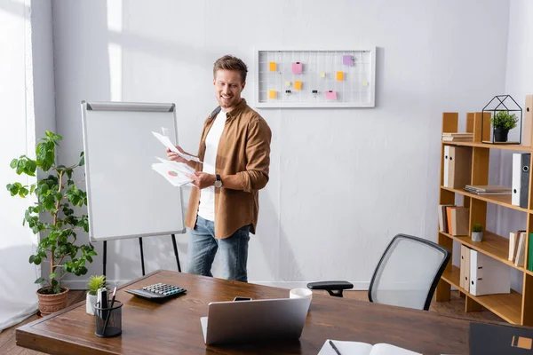 Focus selettivo dell'uomo d'affari che tiene carte vicino al computer portatile e alla calcolatrice sul tavolo dell'ufficio — Foto stock