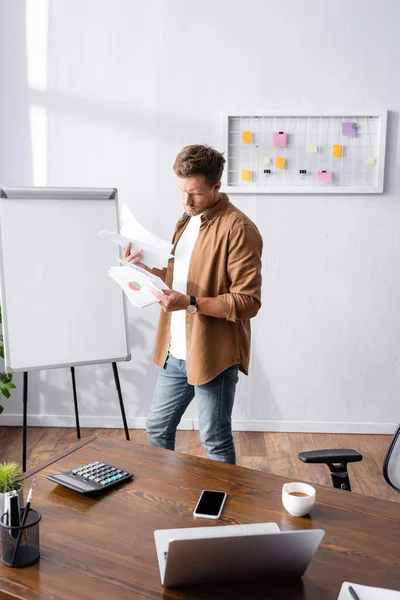 Focus selettivo dell'uomo d'affari che lavora con documenti vicino a gadget e caffè sul tavolo in ufficio — Foto stock