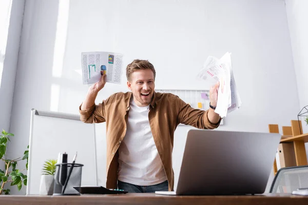 Selective focus of businessman with papers looking at laptop in office — Stock Photo