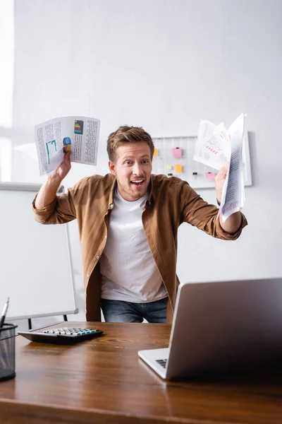 Selektiver Fokus aufgeregter Geschäftsleute mit Dokumenten in der Nähe von Laptop und Taschenrechner auf dem Bürotisch — Stockfoto