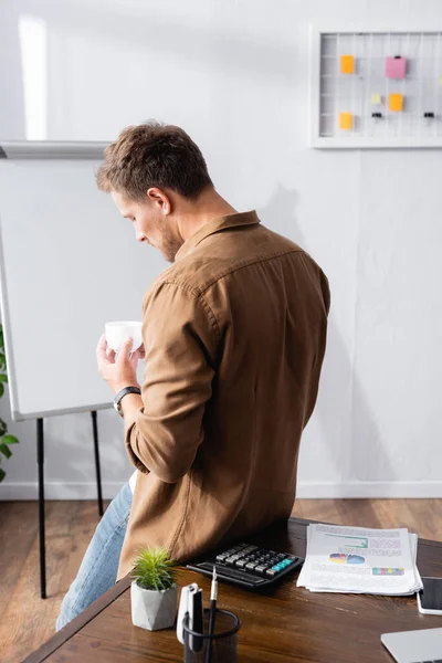 Selective focus of businessman holding cup of coffee near table in office — Stock Photo