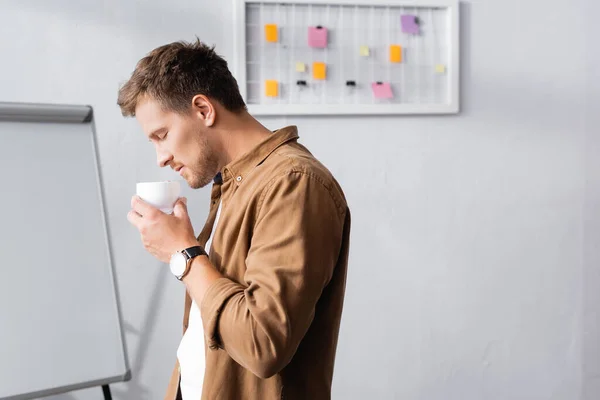 Vista lateral del hombre de negocios sosteniendo la taza de café en la oficina - foto de stock