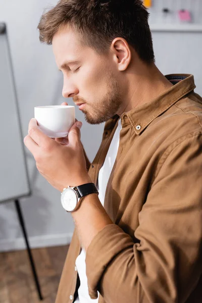 Concentration sélective du jeune homme d'affaires tenant une tasse de café au bureau — Photo de stock