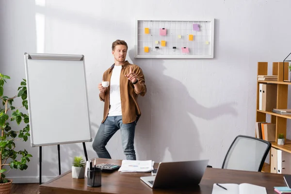 Focus selettivo dell'uomo d'affari con tazza di caffè che ha un'idea vicino alla lavagna bianca e al computer portatile in ufficio — Foto stock