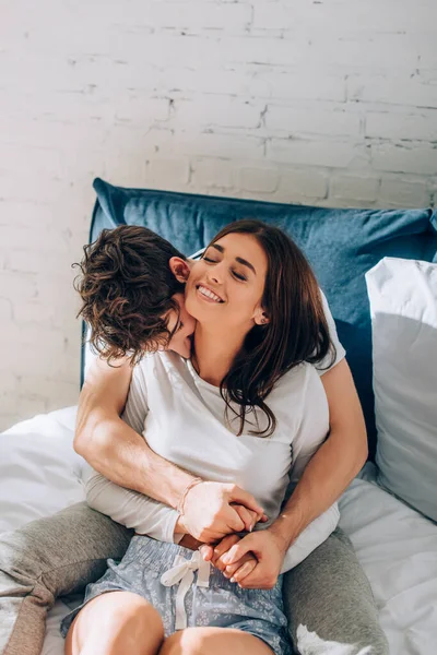 Young man in pajamas embracing girlfriend and kissing in neck on bed — Stock Photo