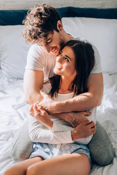 Fröhliches Paar sitzt auf Bett und schaut einander an — Stockfoto