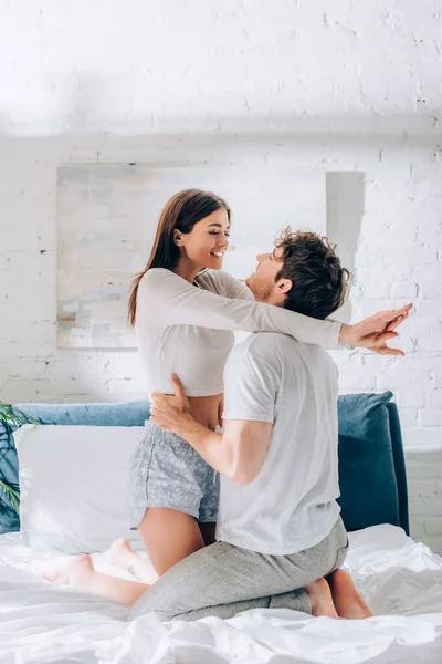 Jeune femme en pyjama embrassant et regardant petit ami sur le lit — Photo de stock