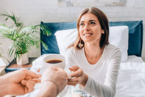Selektiver Fokus der jungen Frau, die ihren Freund anschaut und eine Tasse Kaffee in der Hand hält — Stockfoto
