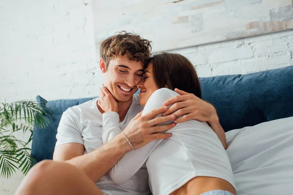 Pareja joven abrazándose y sentándose en la cama - foto de stock