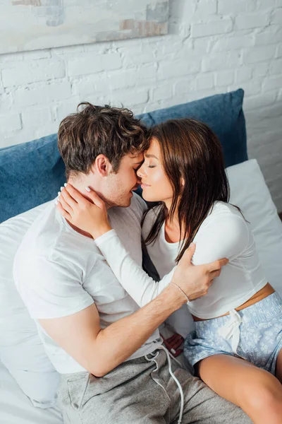Высокий угол обзора пары в пижаме, сидящей на кровати и трогающей друг друга — стоковое фото